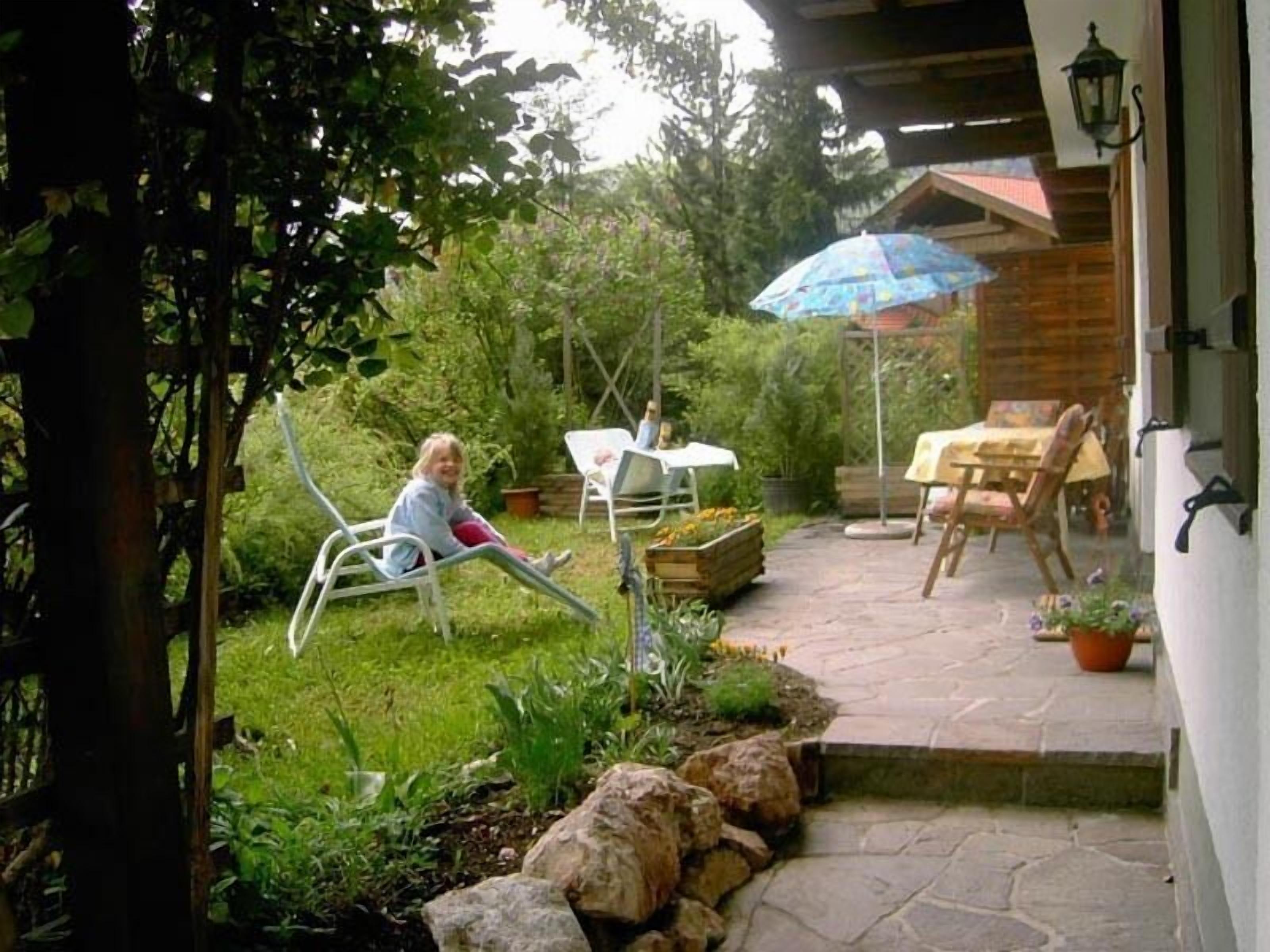 A patio with a table and chairs, a child playing, and a garden area.