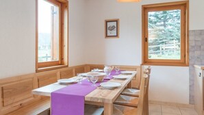 A dining area with a wooden table set for four, benches, and two windows offering views of a forest. - Family 4-room apartment, terrace, near slopes (Le Monêtier-les-Bains)
