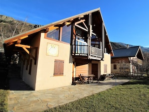A two-story wooden cabin with a balcony, stone pathway, and a clock on the wall.