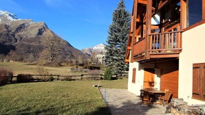 A wooden cabin with a balcony, a stone patio, and a mountain backdrop. - Family 4-room apartment, terrace, near slopes (Le Monêtier-les-Bains)