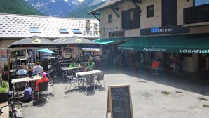 An outdoor café with tables and chairs, a chalkboard menu, and a mountain backdrop. - Family 4-room apartment, terrace, near slopes (Le Monêtier-les-Bains)