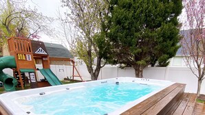 A hot tub with a wooden deck, surrounded by a wooden playhouse and a slide. - Comfortable/Cozy Home (American Fork)