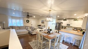 A spacious living area with a dining table, white chairs, a sofa, and a kitchen with white cabinets and appliances. - Comfortable/Cozy Home (American Fork)
