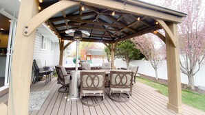 A covered outdoor patio with a grill, seating, and string lights. - Comfortable/Cozy Home (American Fork)