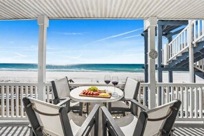 A covered outdoor seating area with a table set for two, overlooking a beach. - 2 Beach Sets ☀️ Beachfront Ocean View | Private Beach | Direct Access ☀️ 125 Perfect Reviews (Santa Rosa Beach)