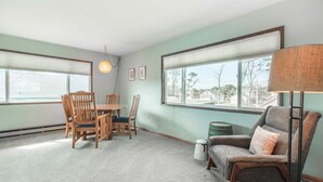 A room with a dining table and chairs, a sofa, a lamp, and large windows with a view. - Aoy Matey · Cute family home, close to beach, fenced yard (Cloverdale)
