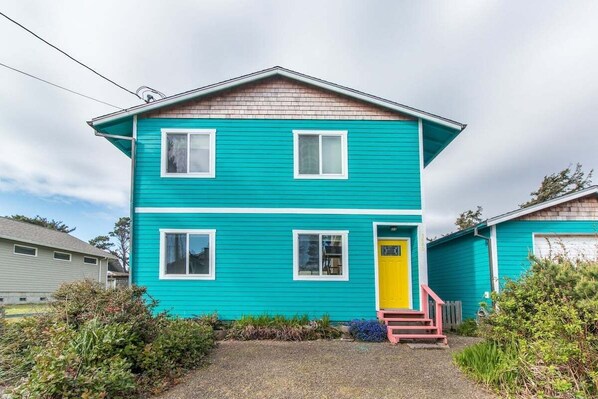 Une maison à deux étages, avec une façade d’un bleu turquoise éclatant et des éléments décoratifs blancs.