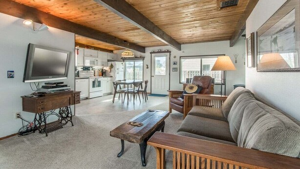 A living room with a wooden ceiling, a television, a sofa, a coffee table, and a dining area with chairs and a table. - Aoy Matey · Cute family home, close to beach, fenced yard (Cloverdale)