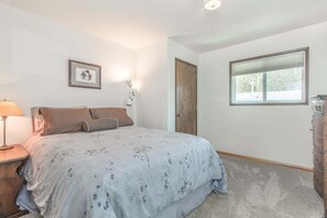 Une chambre à coucher avec un lit, une table de chevet, une commode, une fenêtre et une porte.