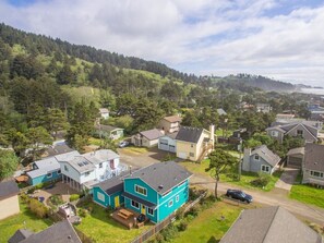 Un quartier résidentiel avec des maisons, une maison bleue qui se distingue particulièrement, et une colline boisée en arrière-plan.