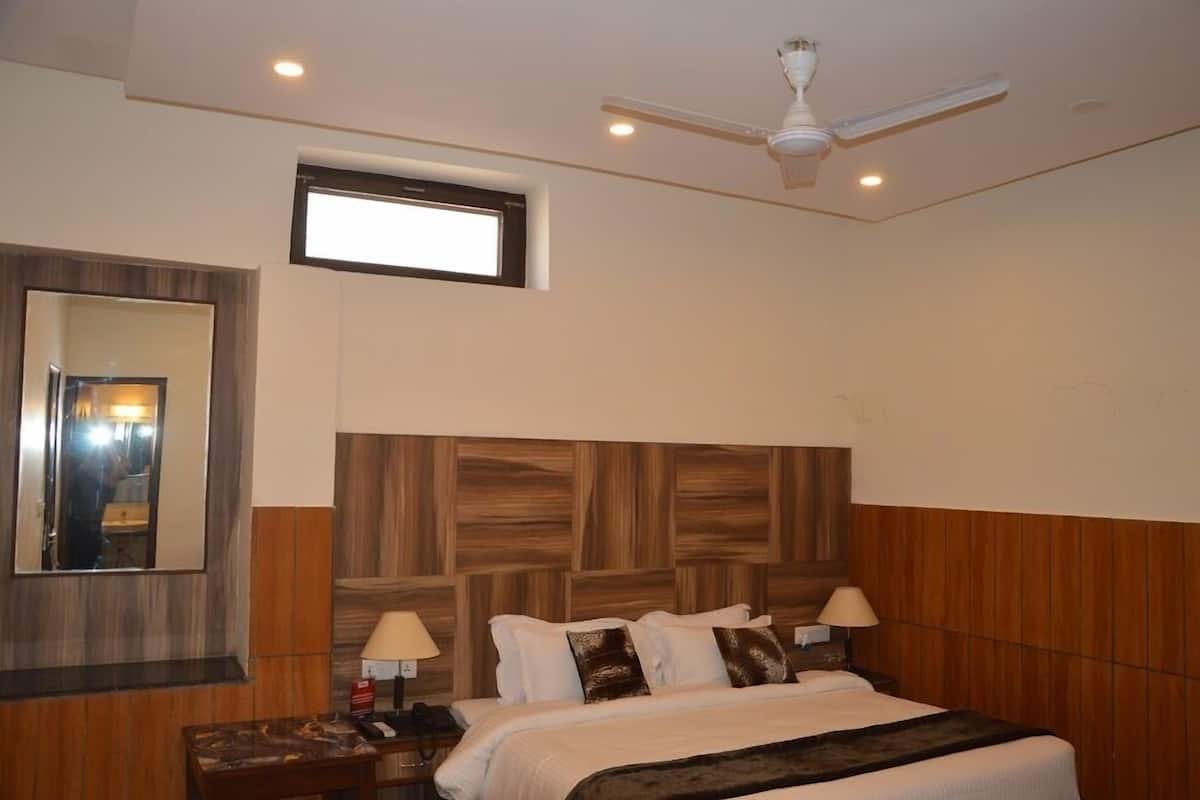 Habitación de hotel con una cama grande, cabecera de madera, dos lámparas de noche, un ventilador de techo y una ventana.