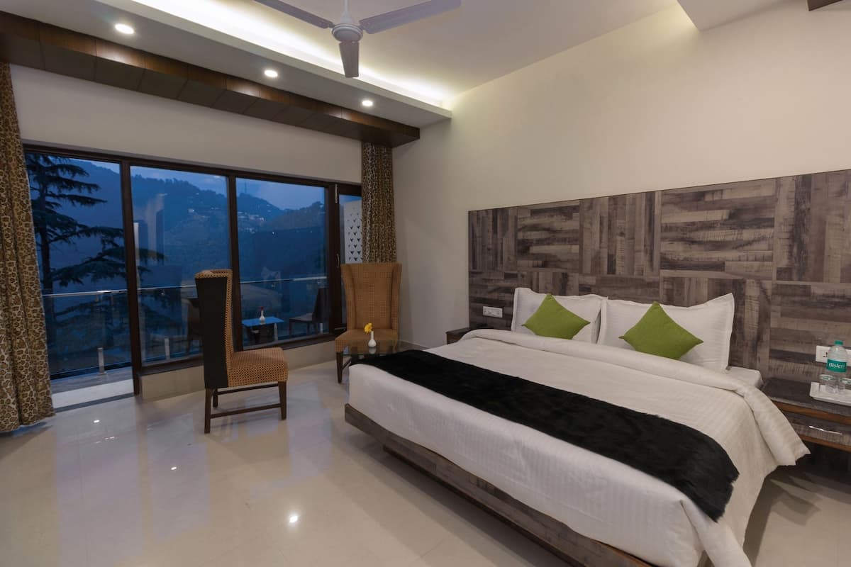 Habitación de hotel moderna con una cama grande, una silla, una mesita de noche y vistas a las montañas a través de amplios ventanales.