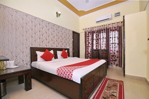 A bedroom with a bed, a nightstand, a wall-mounted lamp, and a window with curtains. - OYO 4069 Morning Star (Dehradun)