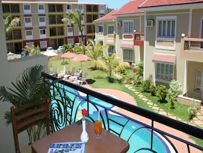 A balcony with a view of a swimming pool, lounge chairs, and a small garden area. - OYO 1254 Hotel Goveia Holiday Homes (Candolim)