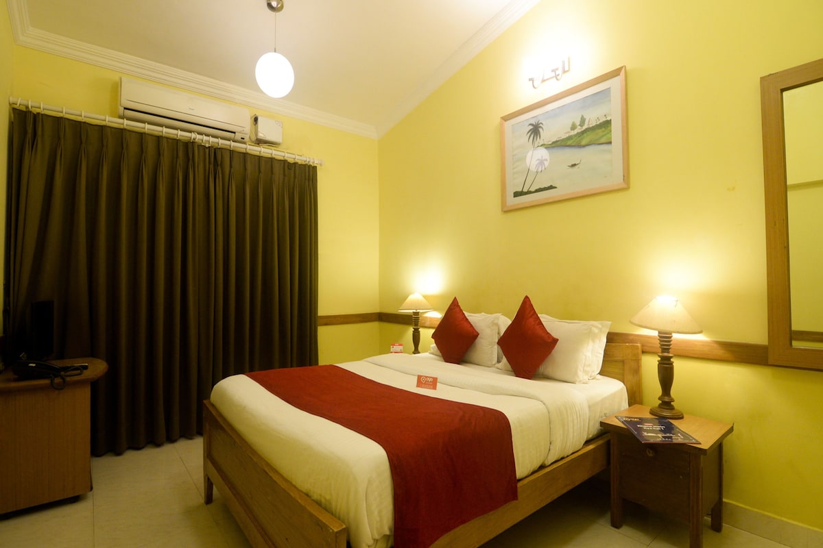 A hotel room with a bed, two bedside lamps, a nightstand, a TV, and a painting on the wall.
