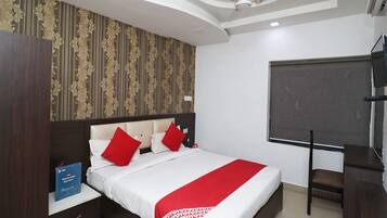 A hotel room with a bed, a desk, a chair, a TV, and a bookshelf.