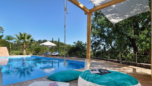 Ein Poolbereich mit Holzterrasse, Liegestühlen und einer Pergola mit weißem Baldachin.