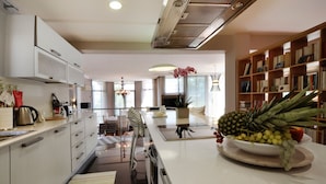 Eine moderne Küche mit weißen Schränken, einer zentralen Kochinsel mit Obstschale und einem Essbereich mit einer Chandelier.