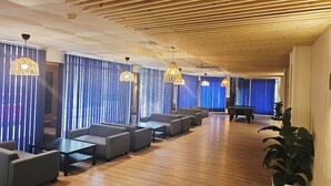 A modern lounge area with wooden ceiling beams, blue vertical blinds, and multiple seating arrangements.