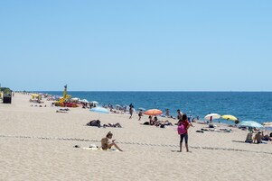 Una playa con gente tomando el sol, sombrillas y sillas de playa.