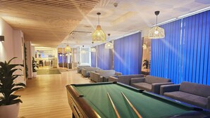 A pool table in a room with a wooden floor, blue curtains, and a seating area with sofas.