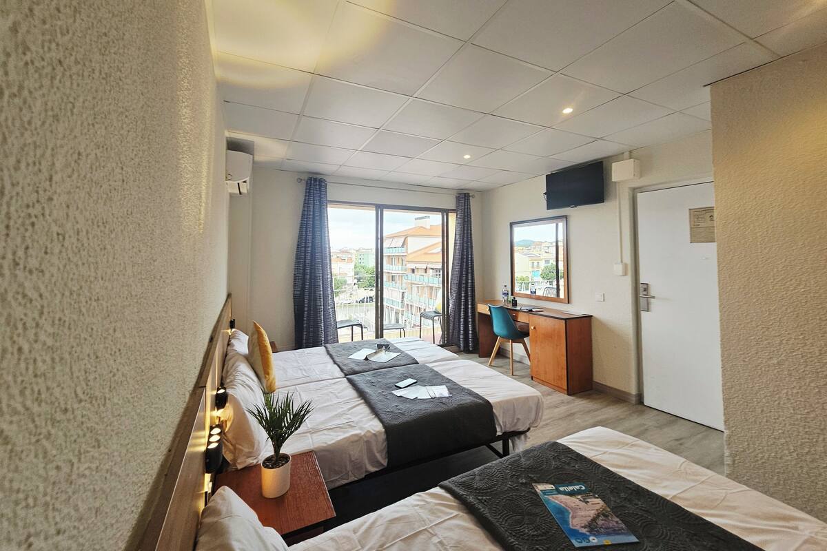 Une chambre d’hôtel avec deux lits, un bureau, une télévision et un balcon avec des rideaux.