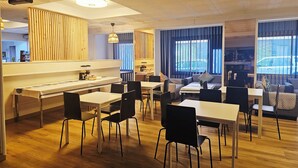 A modern dining area with wooden flooring, black chairs, and white tables.