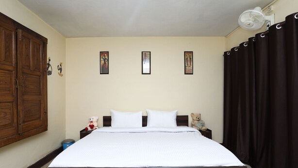 A bedroom with a wooden bed, white bedding, a nightstand with a teddy bear, and a wall-mounted fan. - OYO 12437 Home Valley View 2BHK Villa Gun Hill (Dehradun)