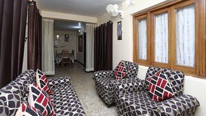 A living room with patterned sofas, a dining area in the background, and a window with curtains. - OYO 12437 Home Valley View 2BHK Villa Gun Hill (Dehradun)