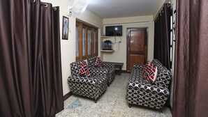 A living room with two patterned sofas, a TV mounted on the wall, and a fan on the ceiling. - OYO 12437 Home Valley View 2BHK Villa Gun Hill (Dehradun)