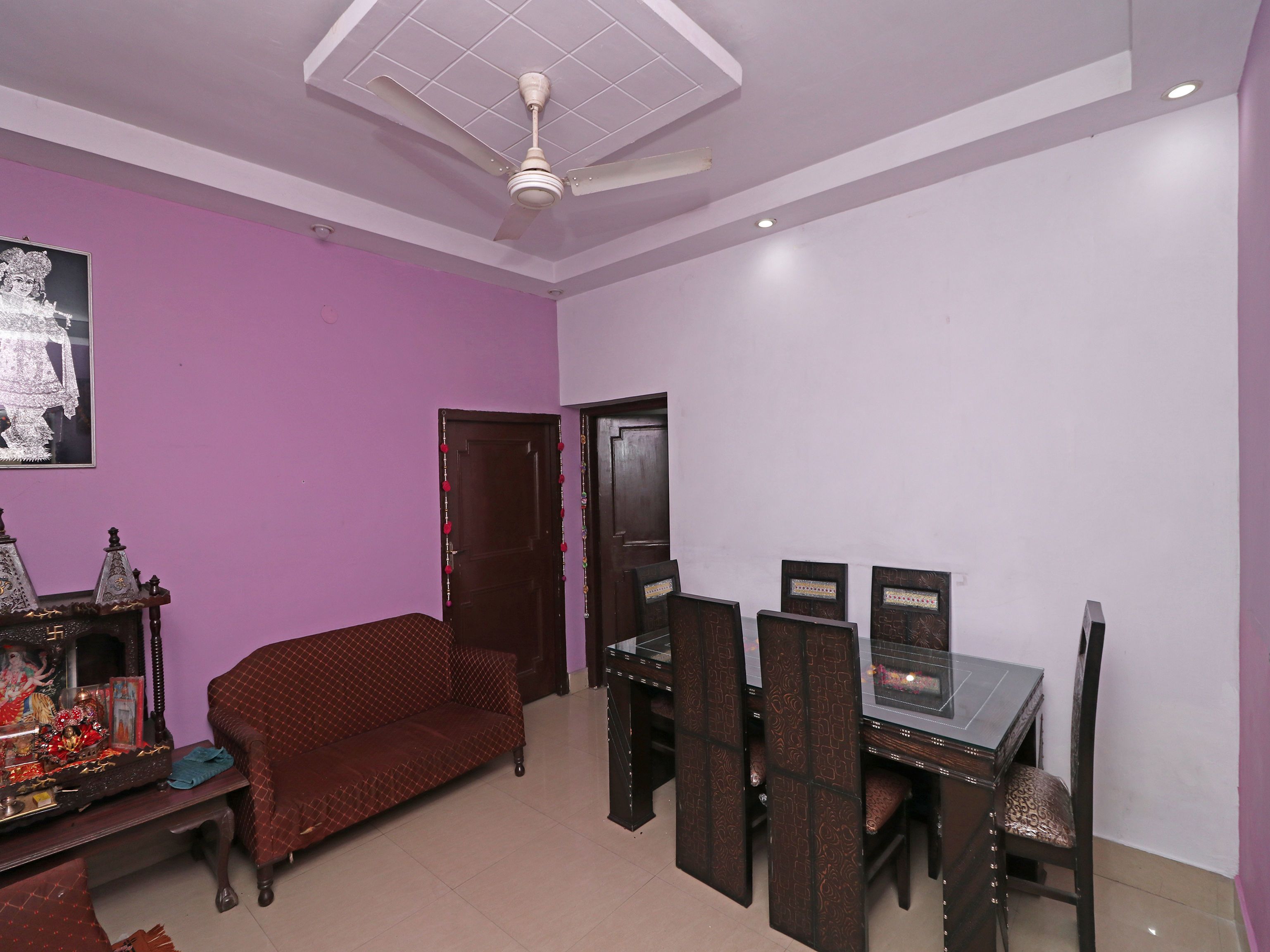 A room with a purple wall, a ceiling fan, a sofa, a dining table with chairs, and a door.