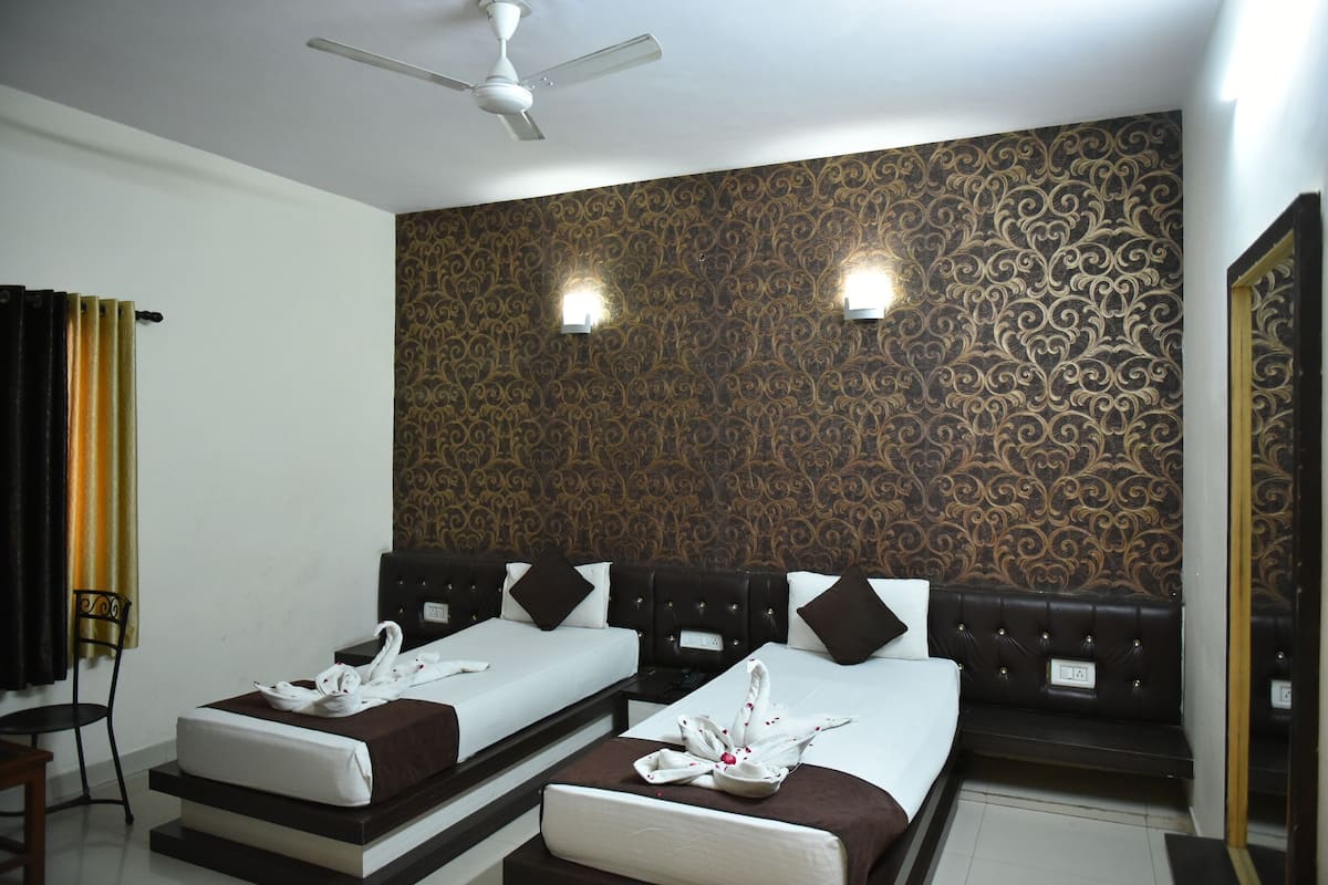 A hotel room with two beds, a ceiling fan, patterned wallpaper, and two wall-mounted lights.