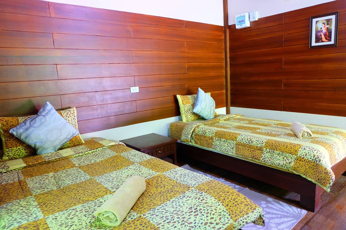 A room with two beds, wooden walls, and a small nightstand.