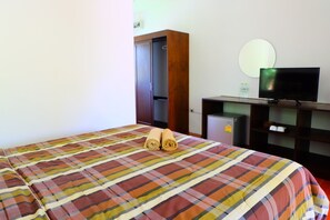 A hotel room with a bed, a TV on a wooden stand, a small fridge, and a wardrobe.
