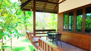 A wooden deck with a table and chairs, surrounded by lush greenery. - Phutien Resort (Chiang Rai)