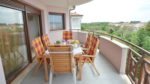 Ein Balkon mit Tisch und Stühlen, Blick auf ein Dorf und eine Schiebeglastür.