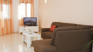 Ein Wohnzimmer mit einem braunen Sofa, einem weißen Couchtisch und einem Fernseher auf einem weißen Schrank.