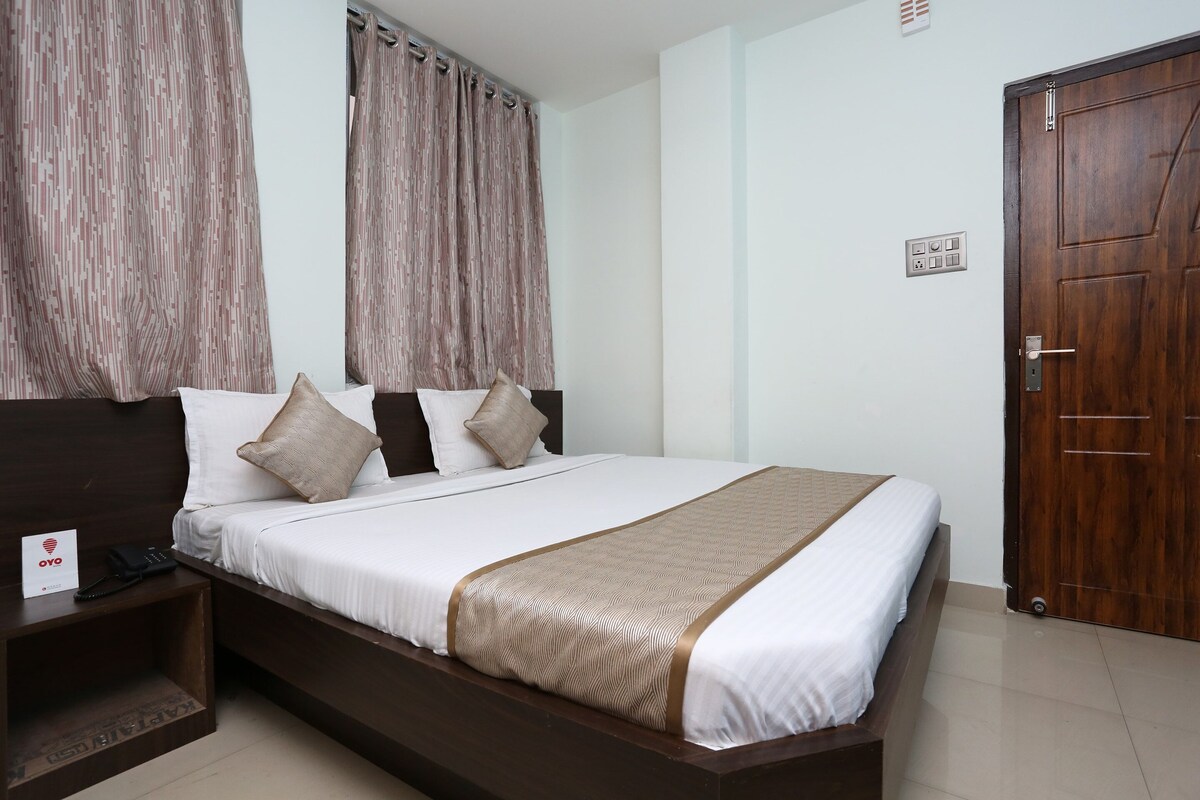 A neatly made bed with a white and brown bedspread, a wooden headboard, and a bedside table with a telephone.