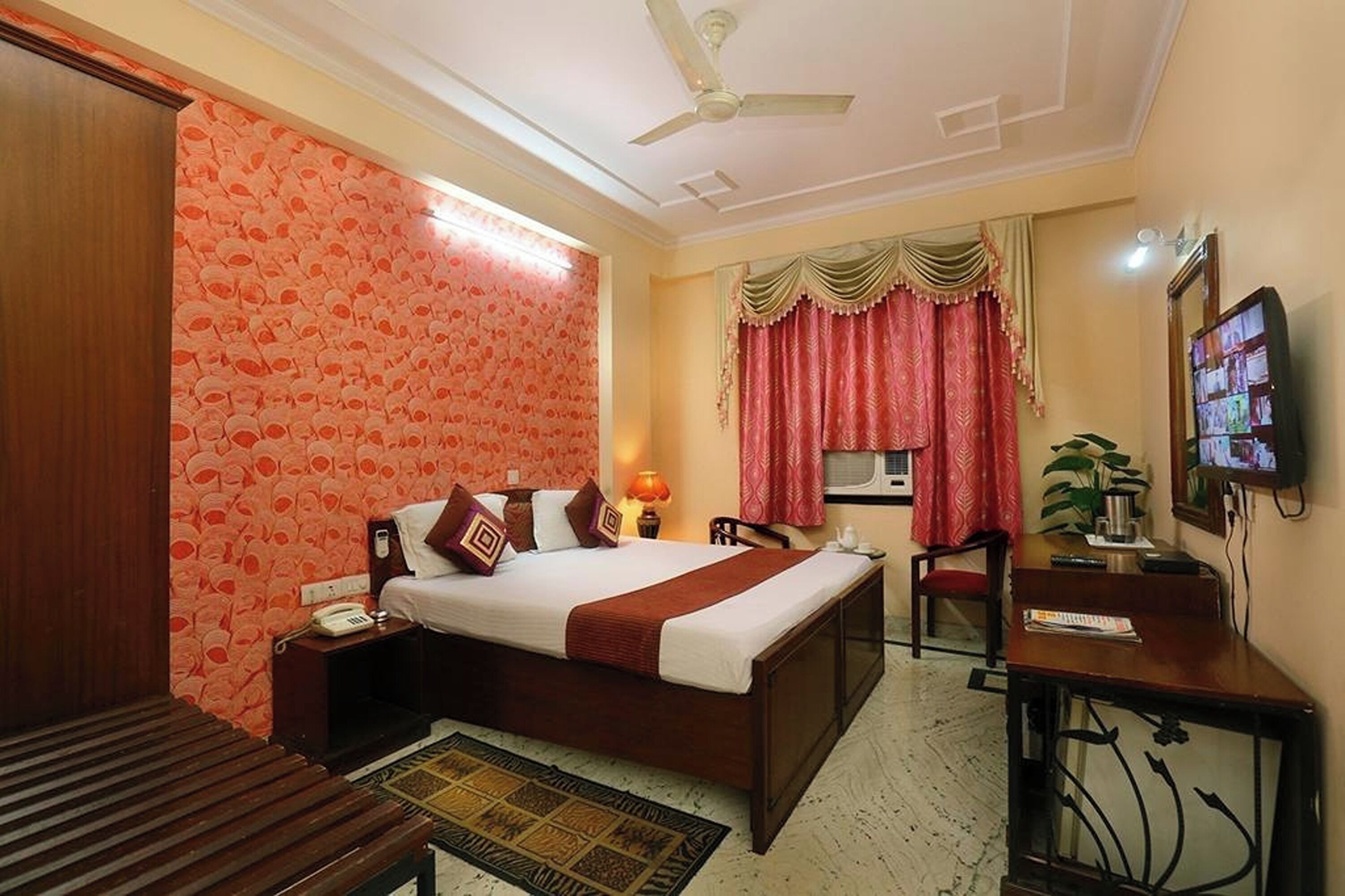 Une chambre d’hôtel comprenant un lit, une table de chevet, une lampe, une télévision, un bureau, une chaise et une petite table avec une plante.