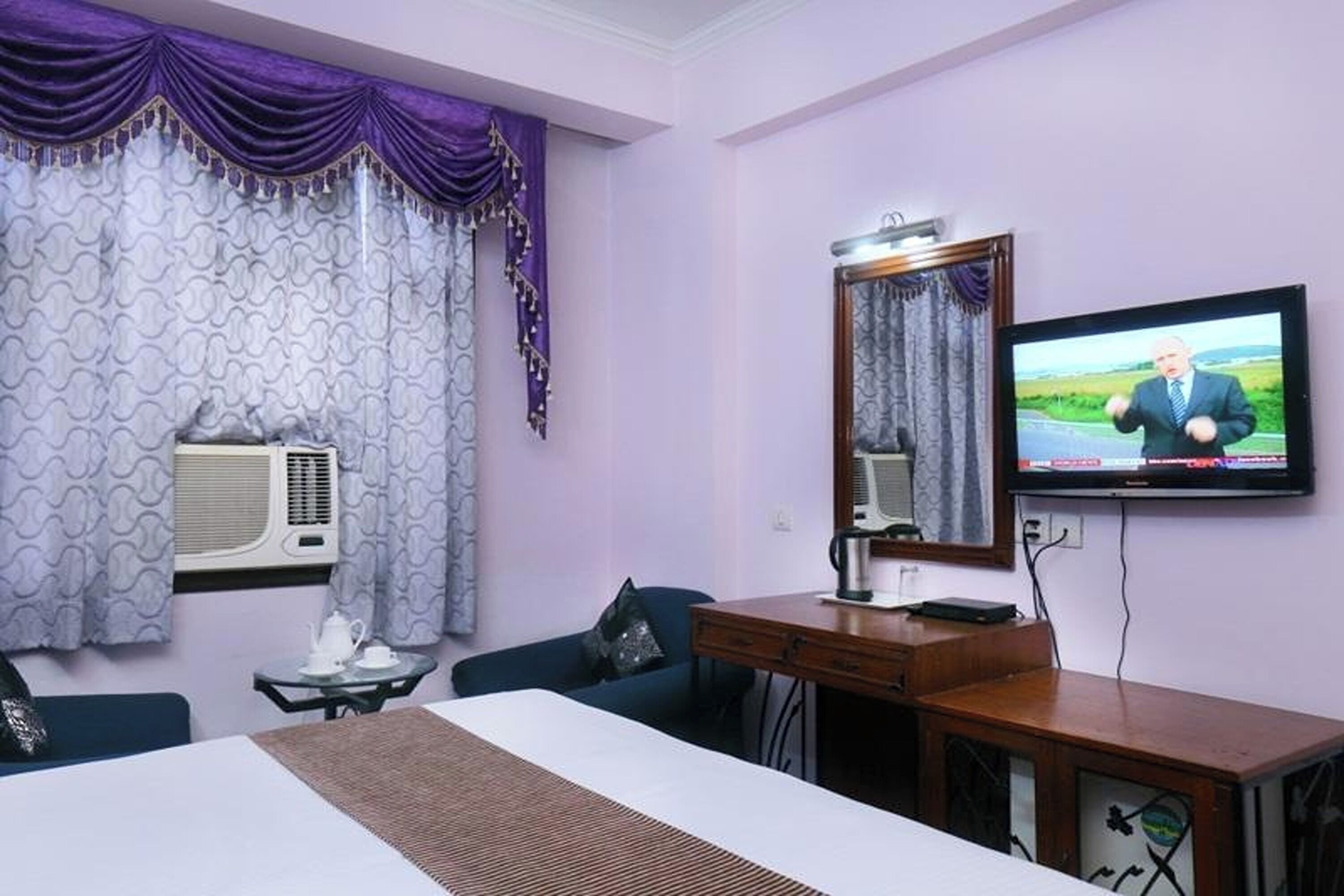 A hotel room with a bed, a desk, a television, and a window with curtains.