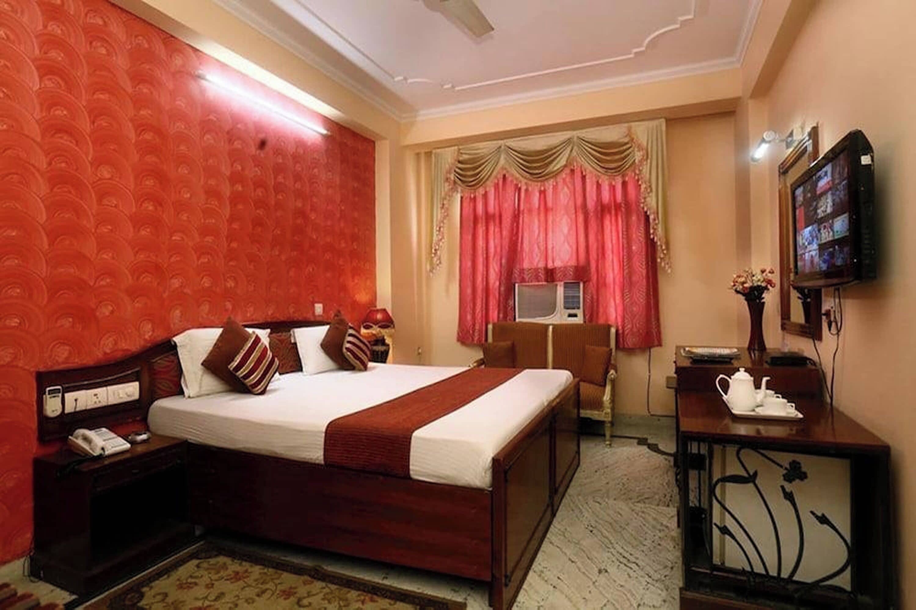 A hotel room with a large bed, a desk with a television, and a telephone.