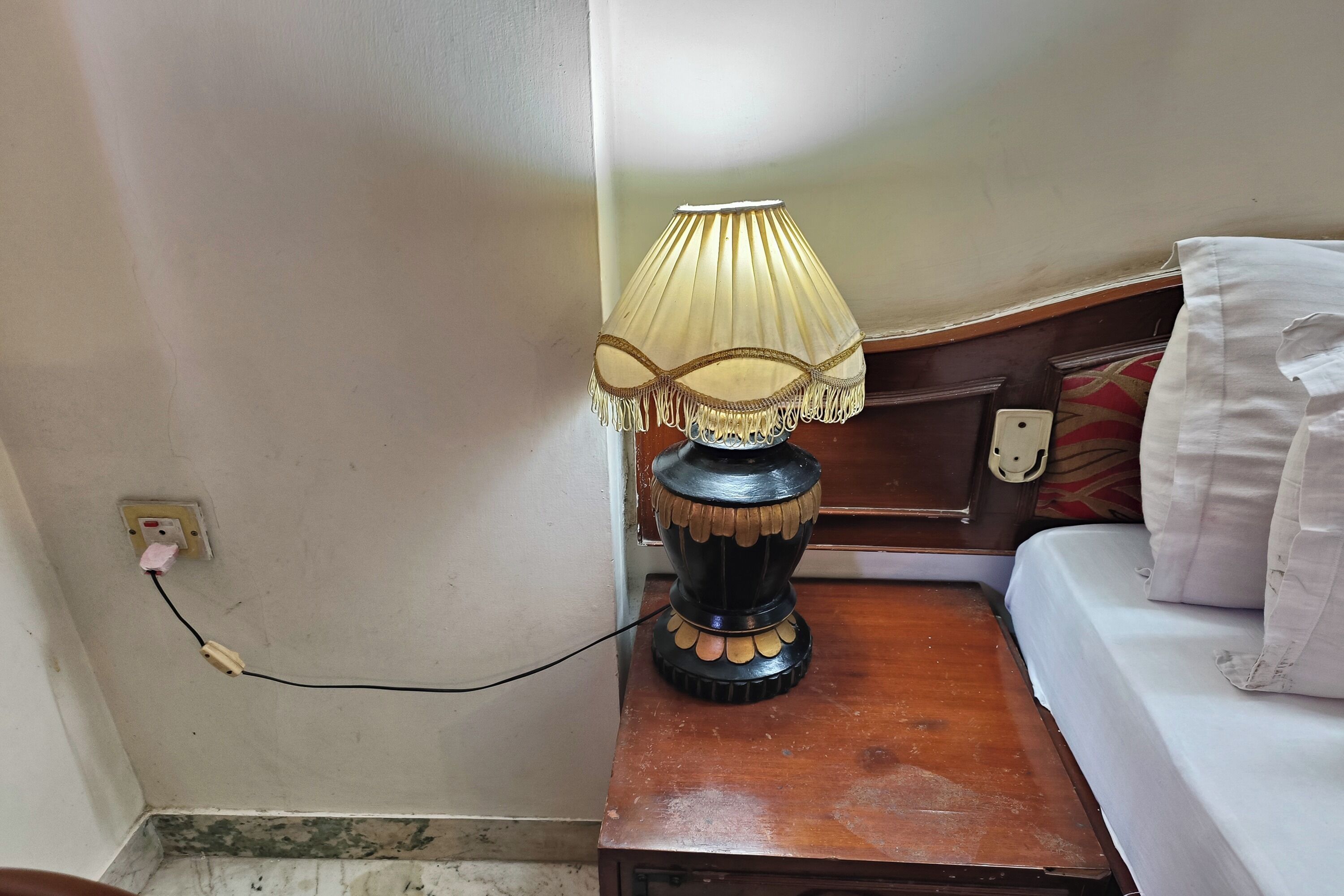 A bedside table with a lamp, a power outlet, and a bed with a pillow.