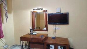A room with a wooden desk, a mirror, a television, and a small table with a kettle and glasses. - Hotel Indraprastha (New Delhi)