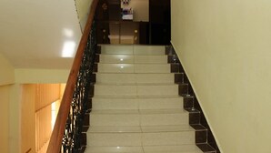 A staircase with a wooden handrail and black railings, leading to a reception area with a sign that reads "GEES IN". - Gees Inn (Nakuru)