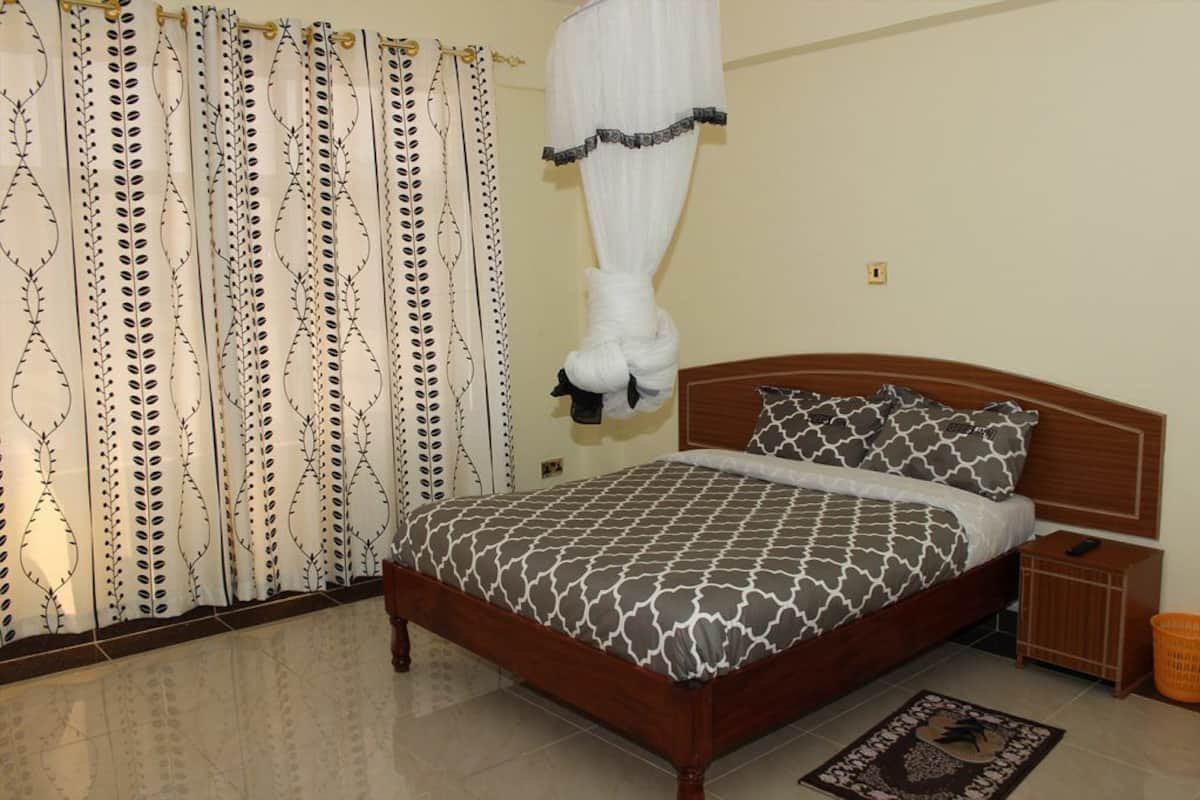 Un dormitorio con cama, cortinas, una mesita de noche y un tocador.