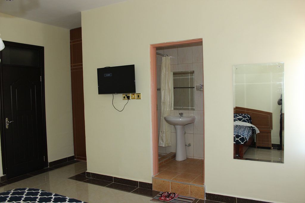 Ein Hotelzimmer mit Bett, Wandfernseher, Waschbecken und Tür.