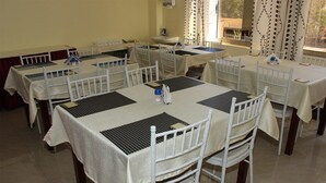 A dining area with multiple tables and chairs, each with a placemat and a small decorative item. - Gees Inn (Nakuru)