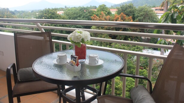 A round glass table with a white vase, two white cups, and a small card holder on a balcony with a metal railing. - Centtro Residences (Los Banos)