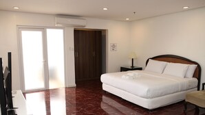 A hotel room with a large bed, a wooden wardrobe, a desk with a lamp, and a TV. - Centtro Residences (Los Banos)
