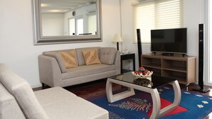 A living room with a sofa, a coffee table with decorative items, a television, and a large mirror on the wall. - Centtro Residences (Los Banos)